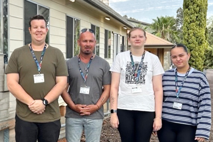 IPROWD students at TAFE NSW Dubbo pose outside a building with their peers. They are standing side by side, wearing lanyards with ID tags attached and smiling at the camera.