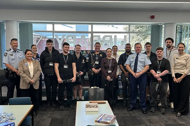 The new IPROWD students stand in the TAFE NSW Nowra campus library, marking the beginning of the 2026 IPROWD program. With them are their teachers, Elders and two police representatives in uniform. Students are wearing casual clothing with lanyards around their necks.