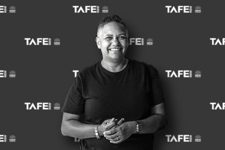 Yvonne O'neill standing in front of a TAFE NSW-branded backdrop, wearing a dark shirt with hands clasped.