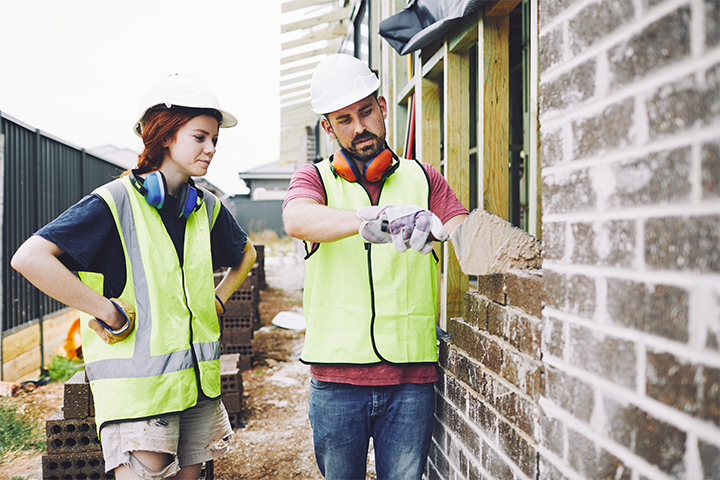 A male teacher is demonstrating bricklaying techniques to a female tradie