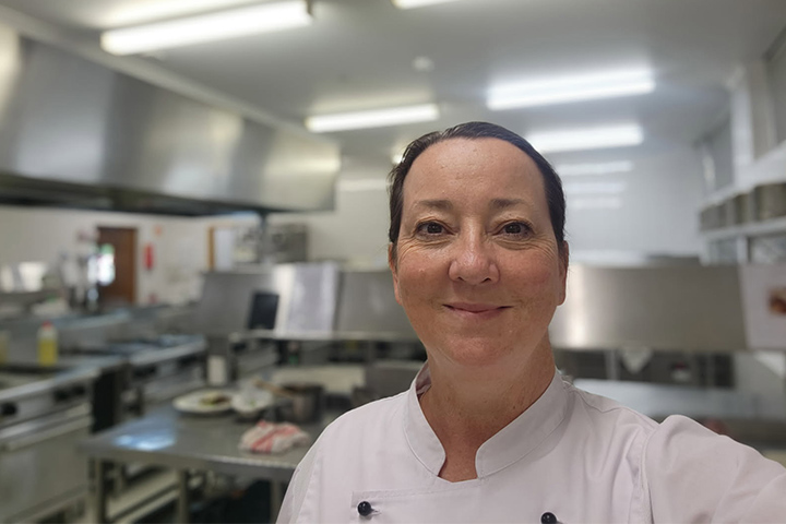 TAFE NSW teacher stands in commercial kitchen, smiling at the camera