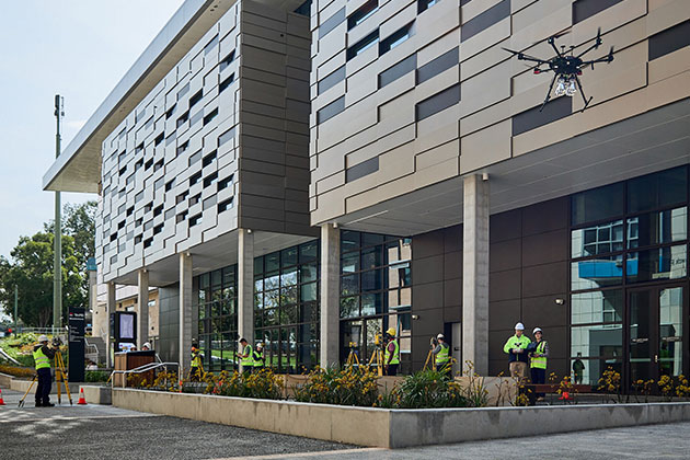 People standing outside a building dressed in high-viz gear, surveying the building. One of the workers is flying a drone in the foreground.