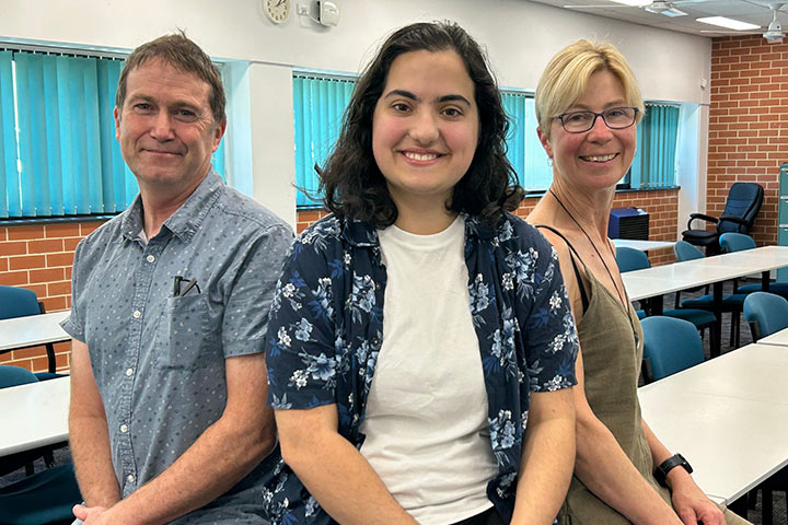 A photo of Elizabeth Poller smiling and sitting on a classroom desk.