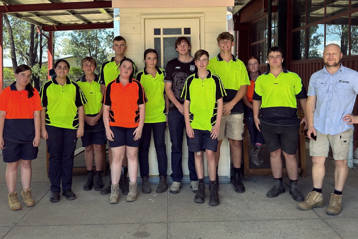 Group of student tradies standing together smiling at the camera while wearing high visibility t-shirts.