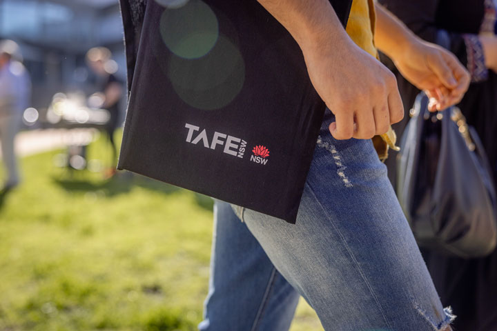 A student walking with a black TAFE NSW tote bag over their shoulder.