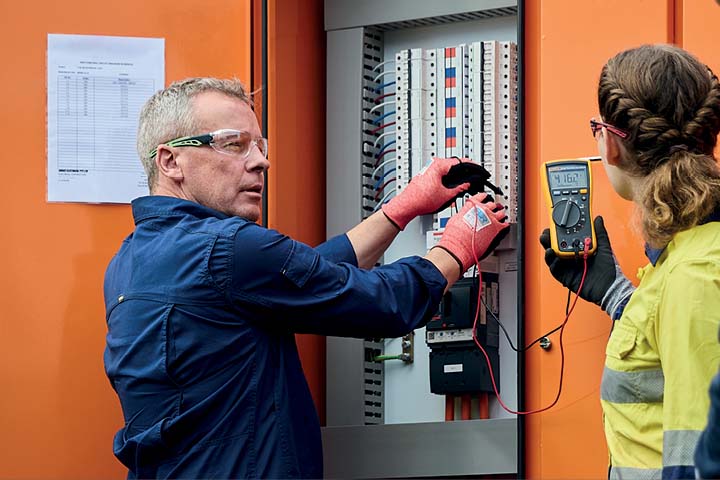 Electrical engineering teacher demonstrating on a powerboard with students observing.