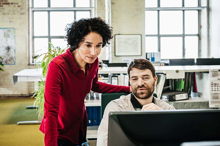 Two colleagues at a desk, one looking over the other's shoulder.