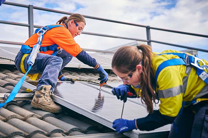Two female solar engineers installing panels on a home's roof. 