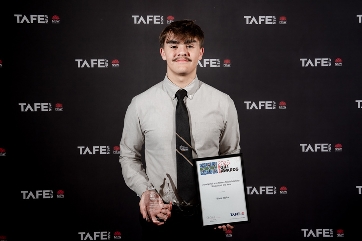 Person holding an award and a certificate in front of a backdrop with multiple TAFE NSW logos.