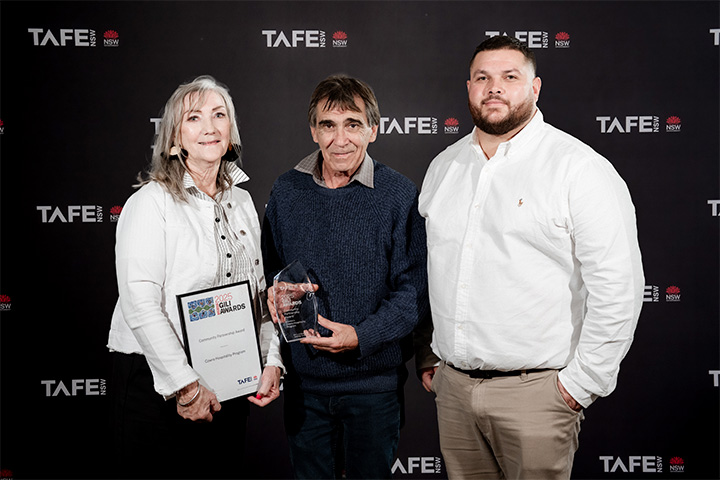 Three individuals standing in front of a TAFE NSW backdrop. One holds a framed certificate reading “2025 Gili Awards Cowra Hospitality Program,” and another holds a clear glass award.