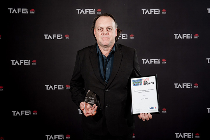 A person holding an award and a certificate in front of a TAFE NSW backdrop. The certificate reads: “2025 Gili Awards – Excellence in Vocational Education and Training – James Barry – TAFE NSW.
