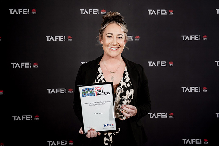 A person holding an award plaque in front of a TAFE NSW backdrop. The plaque reads: “2025 Gili Awards – Aboriginal and Torres Strait Islander Employment Strategy – Katie Spry.”