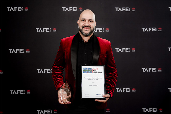 A person holding an award and a certificate in front of a TAFE NSW backdrop. The certificate reads: “2025 Gili Awards – Technology and Business Services – Student of the Year – Mandy Cutmore.”