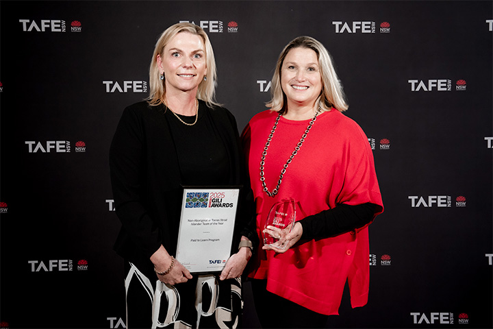 Two individuals standing in front of a TAFE NSW backdrop. One holds a framed certificate reading “2025 Gili Awards – Paid to Learn Program,” and the other holds a glass award.
