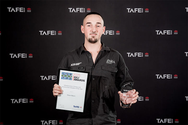 A person holding a framed certificate and a glass award in front of a TAFE NSW backdrop. The certificate reads: “2025 Gili Awards – Outstanding Young and Emerging Talent – Shaun Myers – TAFE NSW.”