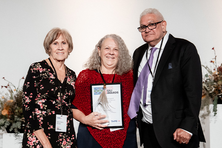 Three people standing together, with the person in the middle holding a framed certificate.