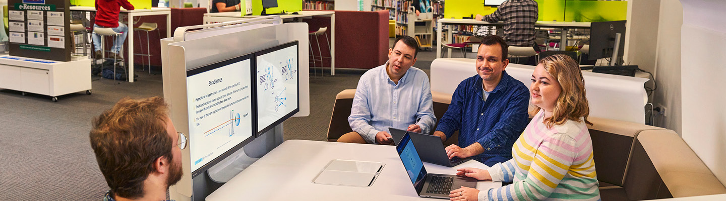 Students gathered around a librarian during an instructional session in a library setting.