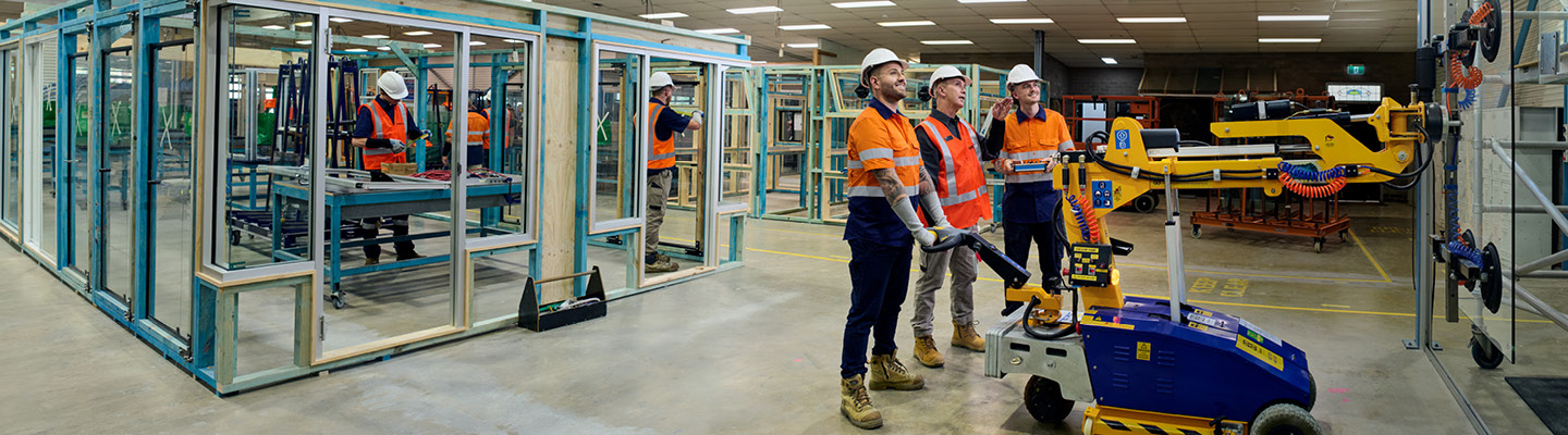 Team conducting a glazing task, applying sealant and positioning glass with safety equipment.