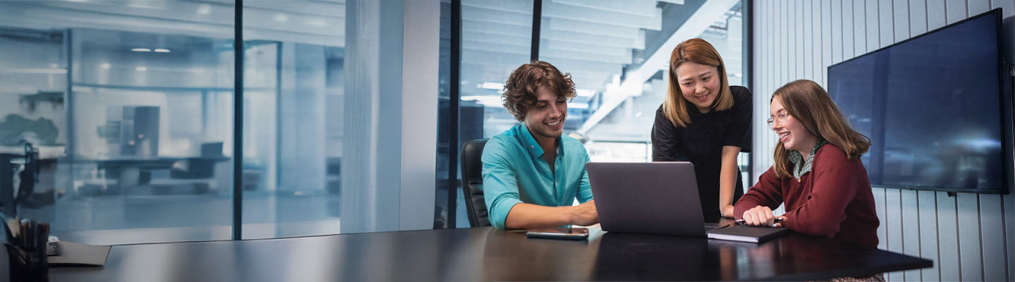 Group of people in a meeting room gathered around a laptop on a table