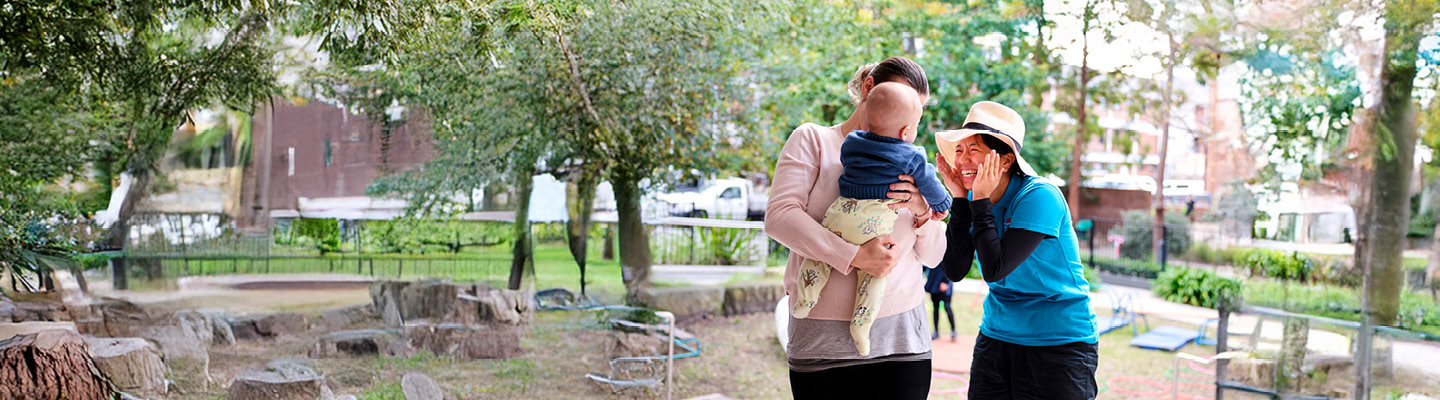 Warm interaction between a parent holding a baby and childcare staff during an outdoor visit