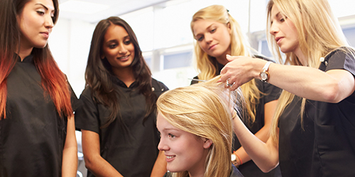 Students in a hairdressing class examining a woman's hair for a suspicious skin spot