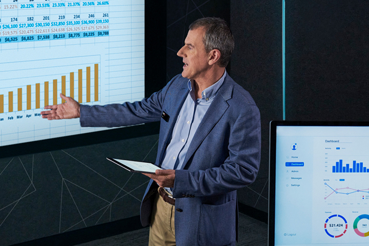A lecturer presenting a spreadsheet with numerical data, percentages, dollar amounts, and the months January through December.