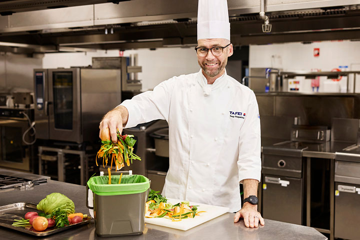 TAFE NSW culinary student practising proper food waste disposal in a commercial kitchen.