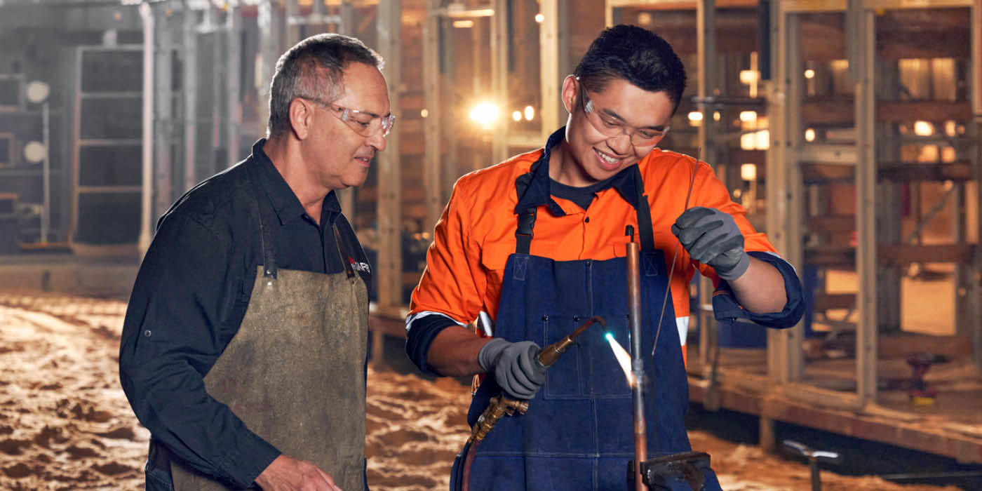 Student welding a pipe with teacher