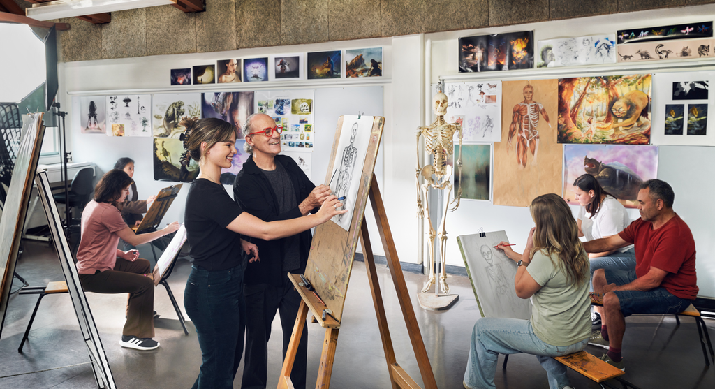 Art class with students seated at easels, drawing and sketching under the guidance of a male instructor with red glasses. Various anatomical and fantasy artwork is displayed on the walls, and a skeleton model stands in the background. The atmosphere is collaborative and focused.