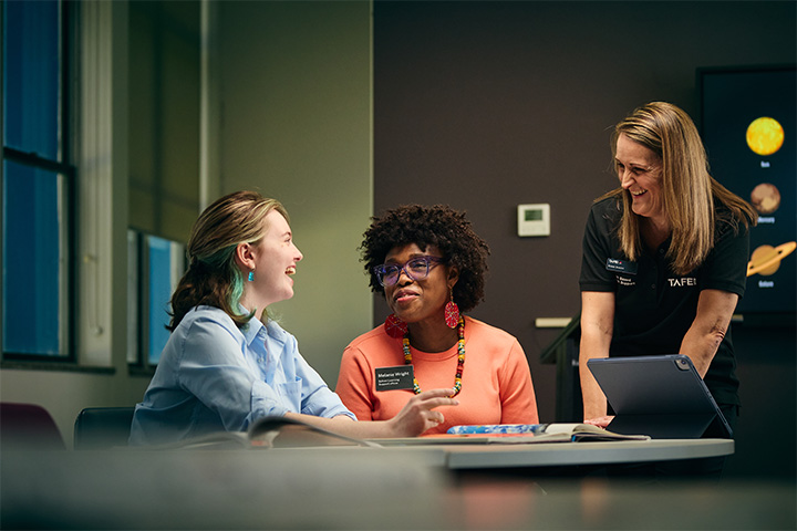 Students and teacher discussing over laptop in classroom setting