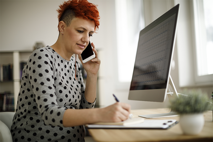 A lady talks on the phone as she writes down information on a form