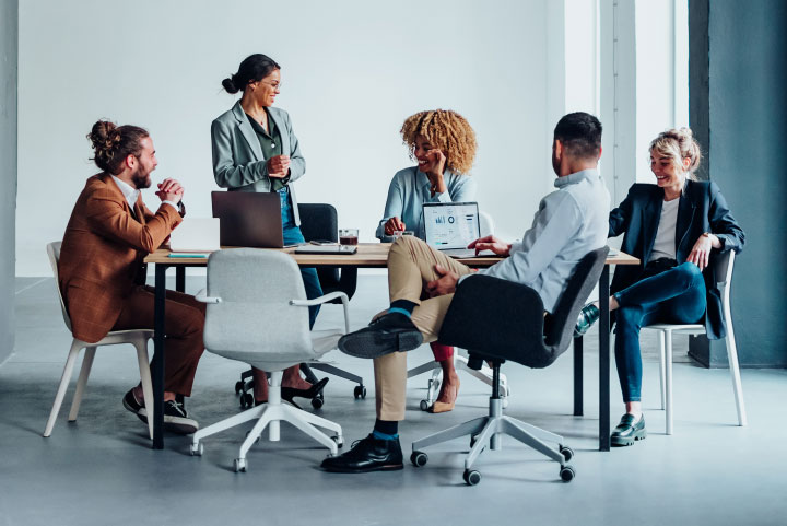 Five people sitting around a table in an office, having a discussion and smiling.