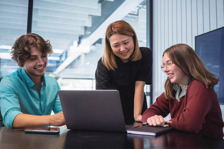 A career advisor stands and gives advice to two adult students in a meeting room.