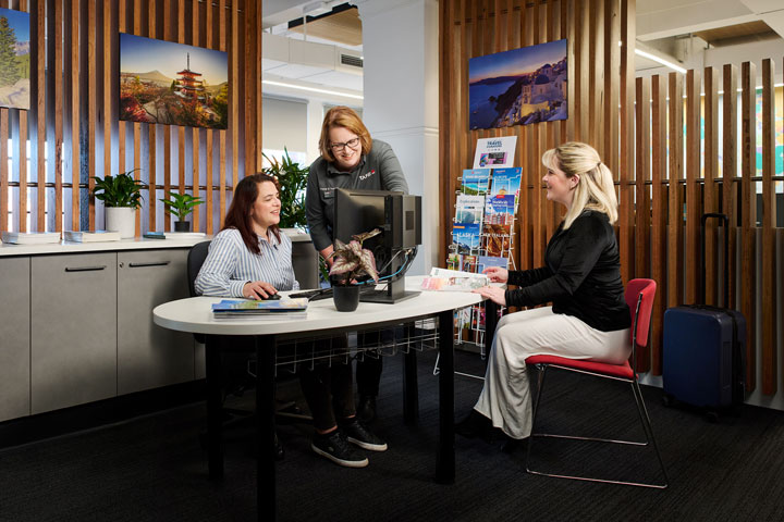 Tourism student and teacher assisting customer in travel agency.