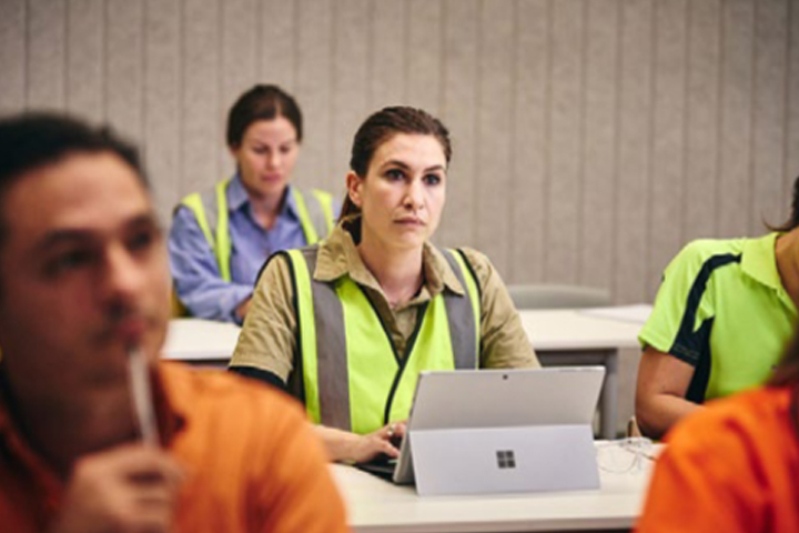 Group of workers in high-visibility vests attending a training session with laptops