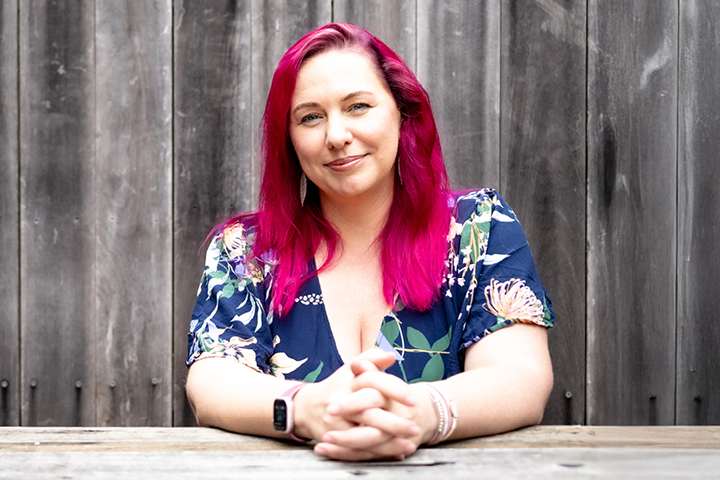 Frances Quinn, Women in Business webinar presenter on 'Prioritise What Matters: Purposeful Productivity,' seated at a wooden table wearing a floral dress, with vertical wooden panels in the background.