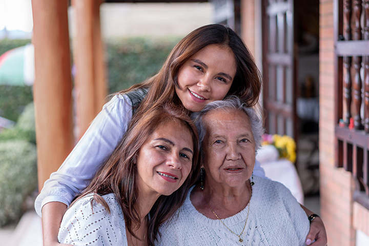 Three individuals in an outdoor setting with wooden columns and a flower-adorned table engage in casual conversation, representing diverse generational perspectives relevant to marketing behaviour analysis.