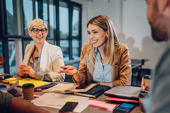 Group of professionals collaborate around a table with laptops, notebooks, and sticky notes during a marketing workshop focused on defining Unique Selling Points and analysing competitor insights.