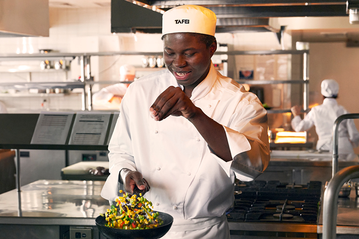Professional chef in white uniform garnishing a colorful salad in a commercial kitchen.