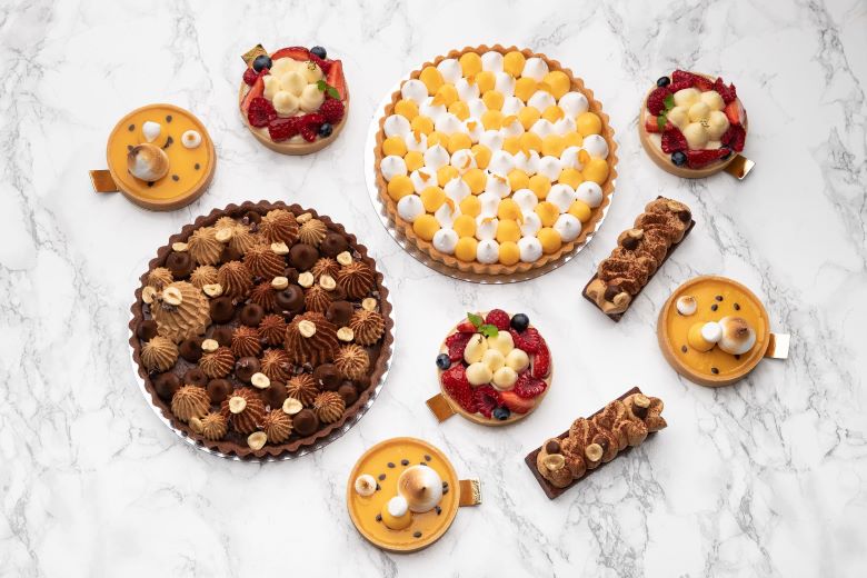 An assortment of professional tortes and tarts carefully displayed on a marble bench top.