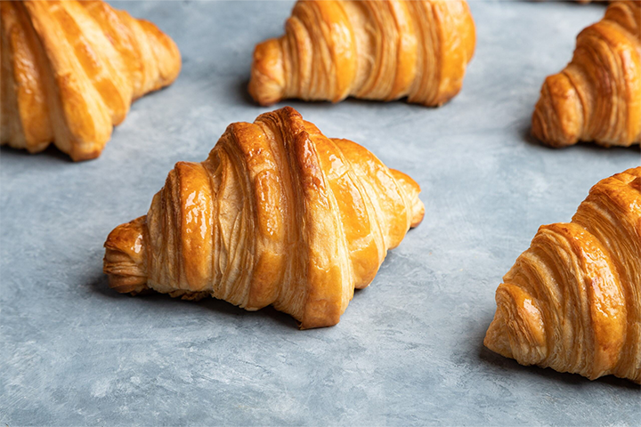 A baking tray is lined with rows of freshly baked, golden croissants