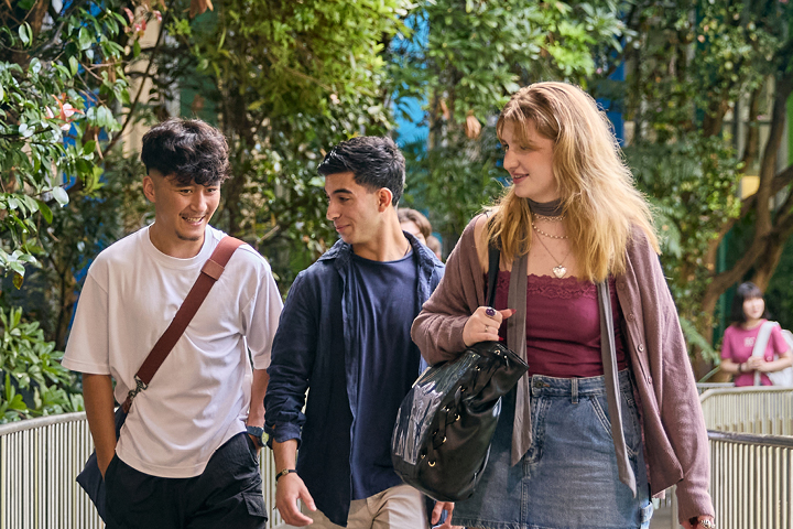 A group of three students are walking through Bradfield campus. There are trees and greenery around.