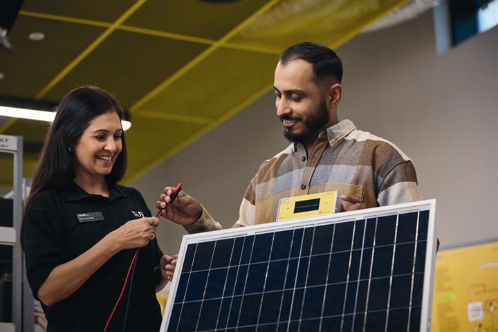 Two individuals work with a solar panel and electrical testing equipment in a modern training facility, demonstrating renewable energy skills as part of TAFE NSW Centres of Excellence in Manufacturing.