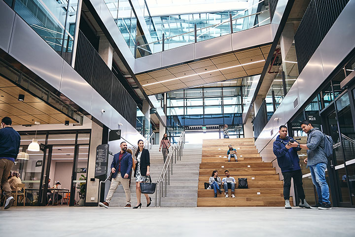 TAFE NSW campus atrium and concrete staircase where students and staff are en route, while others sit, chat and work on the adjacent, tiered wooden steps