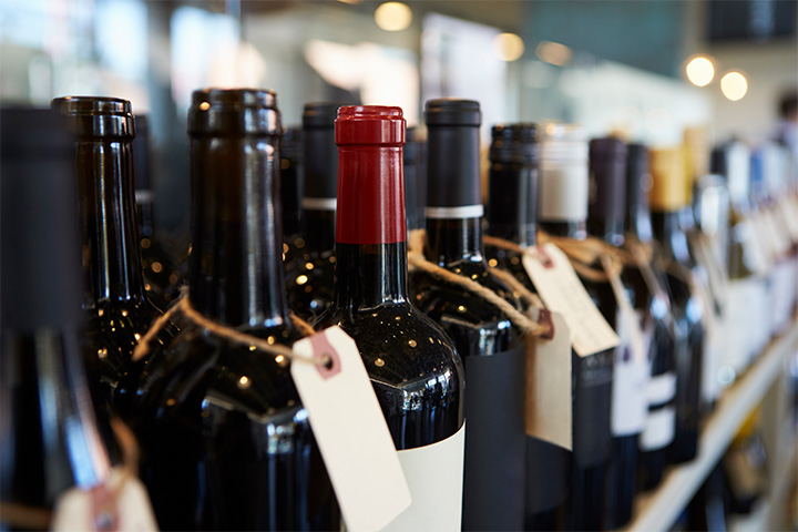 Dark-coloured wine bottles lined up on a shelf, each with a tag around its neck.
