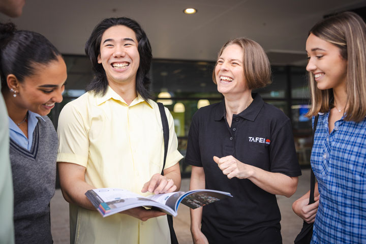 Students are gathered together with a TAFE NSW staff member. They are smiling and laughing while looking at a brochure that shows the range of courses that are available to them in their final years, or after high school.
