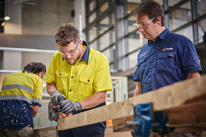 Carpentry student sawing wood with ɫֱteacher supervising