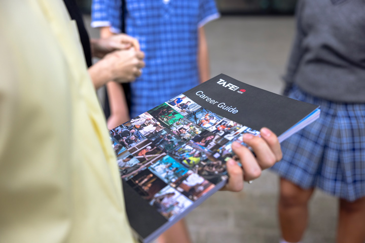 Group of students standing together, with one student holding a 'TAFE NSW Career Guide' booklet featuring images of various career paths and activities on the cover.