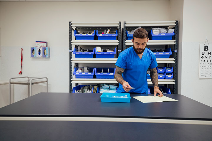 Young Indigenous male healthcare worker in scrubs, carefully examining blood samples in a clinic.