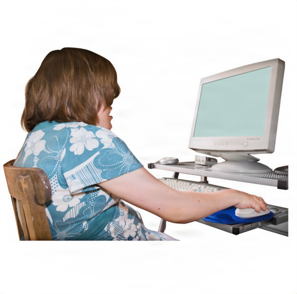 A person in a floral shirt using a desktop computer with an adaptive keyboard.